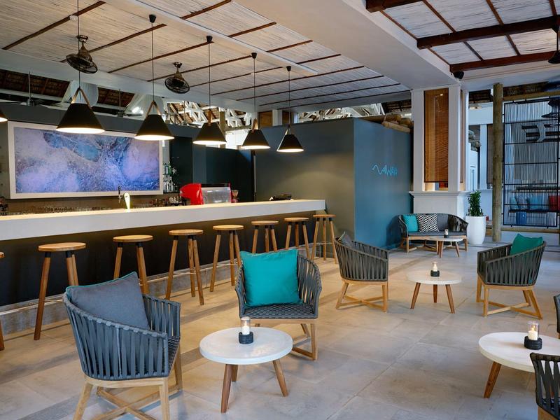 Lounge moderna de hotel con barra, áreas de asientos y elegantes sillones azules bajo techo de madera