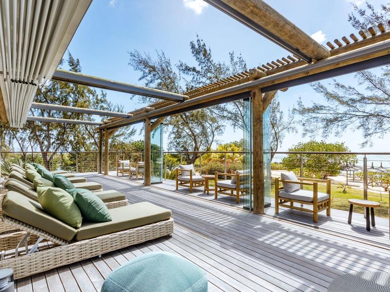 Espaciosa terraza con tumbonas y mesas, rodeada de árboles y vista al mar.