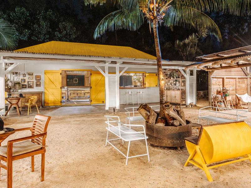 Área al aire libre nocturna en hotel con asientos, fogata y decoración rústica bajo luz cálida.