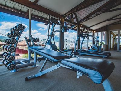 Helles Fitnessstudio mit Gewichten, Bankdrückstation und großen Fenstern mit Außenblick.