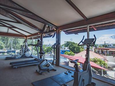 Überdachter Fitnessbereich mit Laufbändern und Fahrradergometern, offen mit Blick auf Häuser.