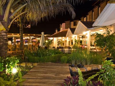 Nächtliche Außenansicht eines Restaurants mit warmen Lichtern, Pflanzen und Holzsteg im Vordergrund.