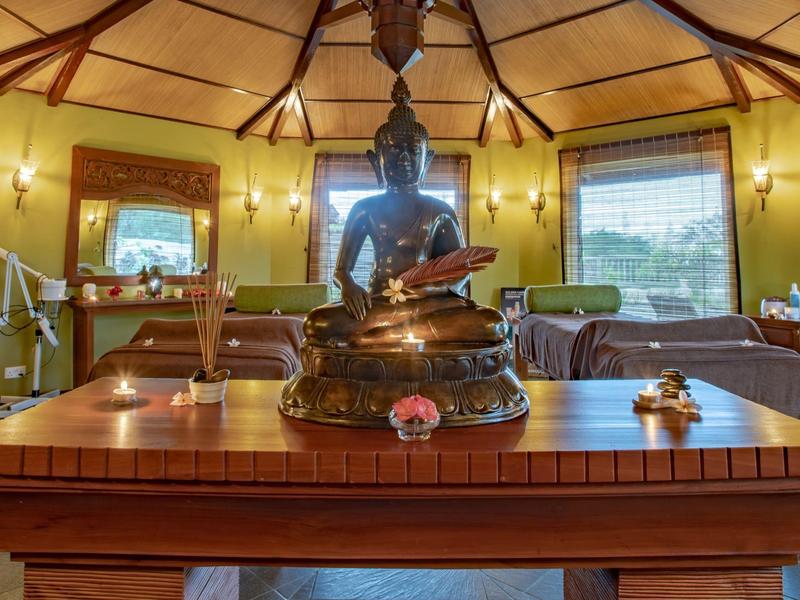 Dřevěný stůl s sochou Buddhy v útulné, teple osvětlené místnosti s postelemi.