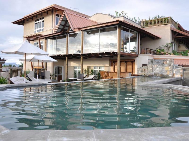 Moderní hotelový komplex s velkým venkovním bazénem a sluneční terasou pod modrou oblohou.