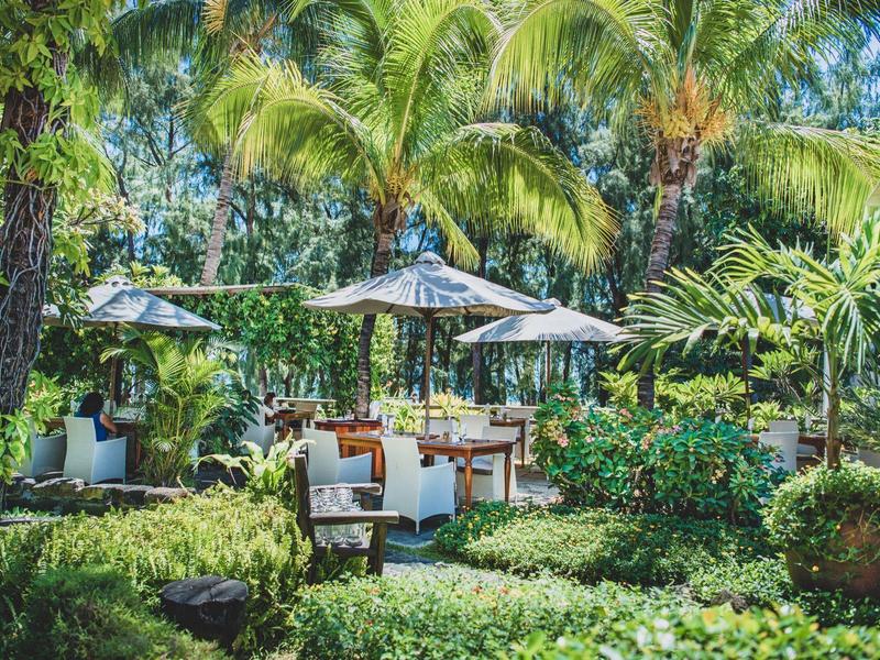 Zelená zahradní plocha s útulným posezením a slunečníky pod palmami.