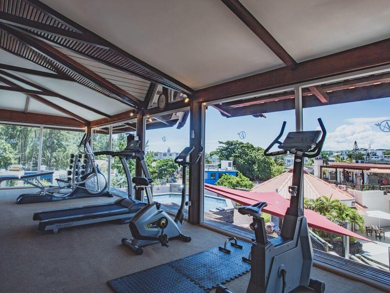 Posilovna s běžeckými pásy a rotopedy s výhledem na střechy a stromy venku.