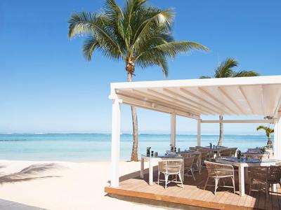 Strand mit weißem Sand, klarem blauen Meer, Palmen und einem offenen Restaurant mit Holzstühlen.