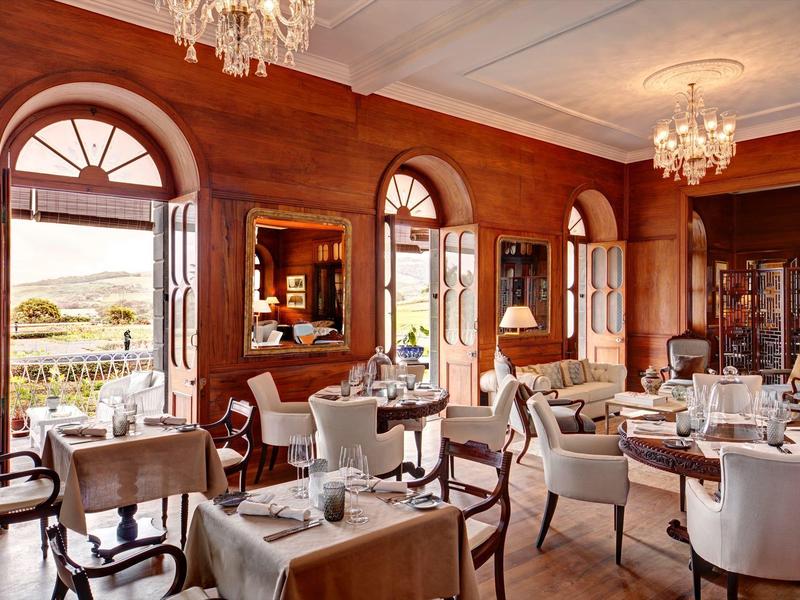 Elegantes Restaurant mit Holzwänden, weißen Tischtüchern, Kronleuchtern und großen Fensterbögen.