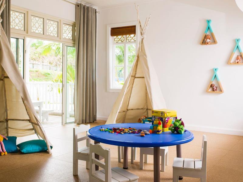 Heller Kinderraum mit zwei Tipi-Zelten, rundem blauen Spieltisch und drei Wanddekorationen.