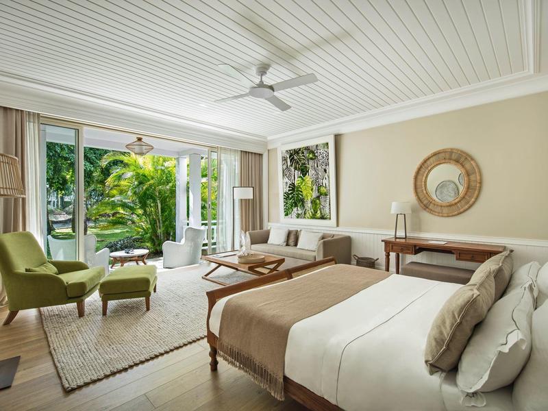 Helles Schlafzimmer mit großem Bett, grünen Sesseln, Holzmöbeln und großem Fenster zum Garten.