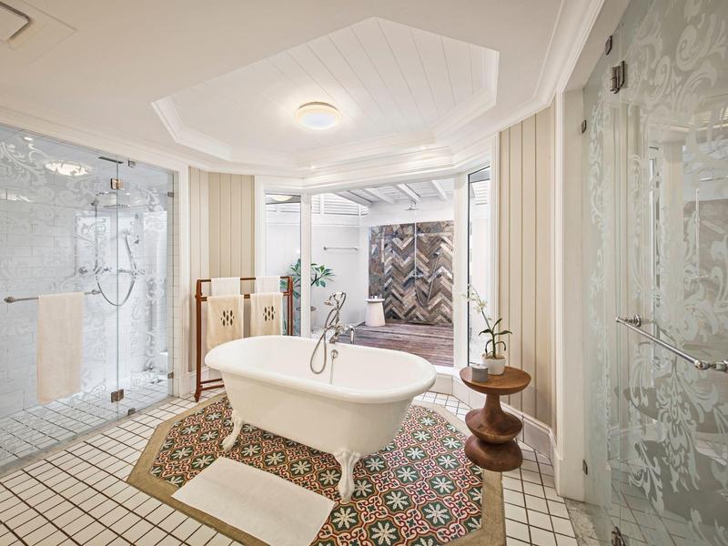 Helles Badezimmer mit freistehender Badewanne, Glasduschen, buntem Teppich und modernen Armaturen.