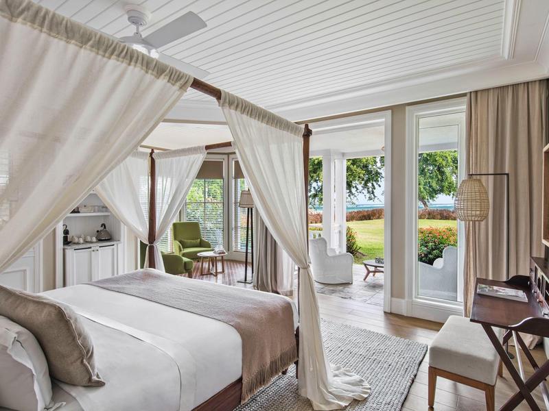 Helles Schlafzimmer mit Himmelbett, Glasfront und Blick auf grüne Pflanzen und Terrasse.