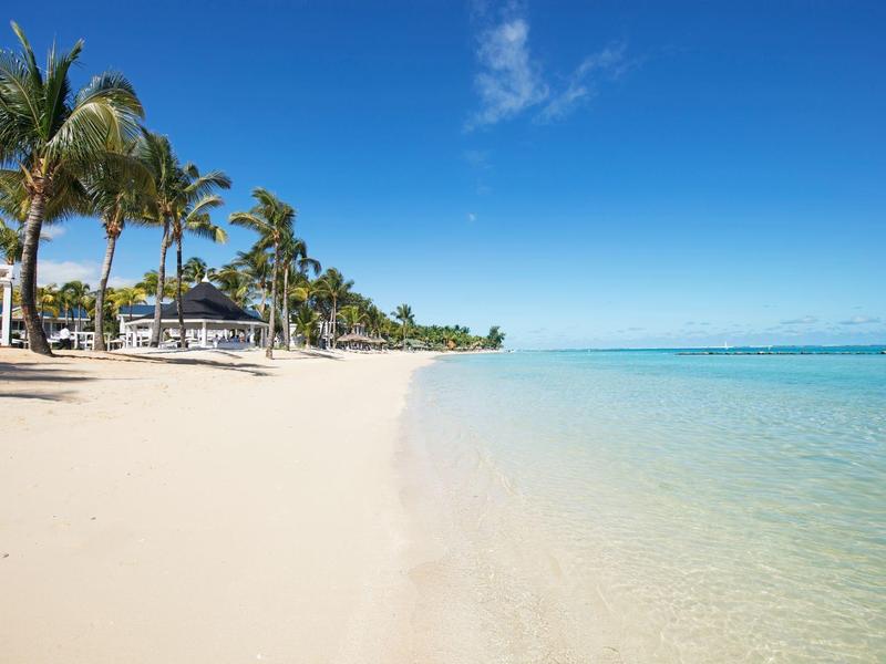 Weißer Sandstrand mit Palmen, klarem türkisfarbenem Wasser und blauem Himmel.