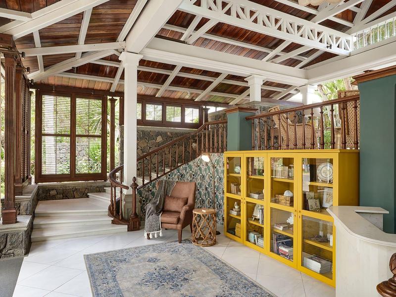 Světlá hotelová hala s dřevěným stropem, žlutou knihovnou a vintage nábytkem.