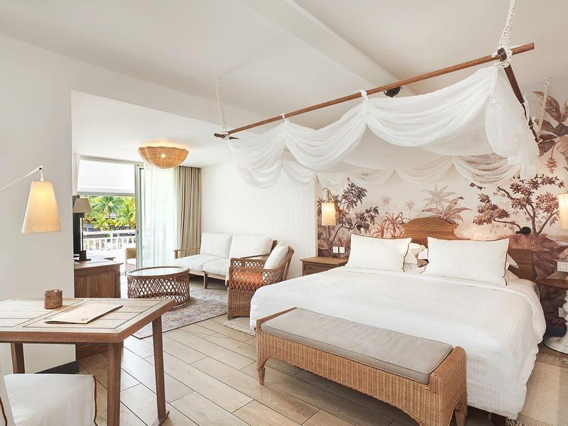 Světly hotelový pokoj s postelí s baldachýnem, dřevěnými prvky a pohodlným posezením u okna.