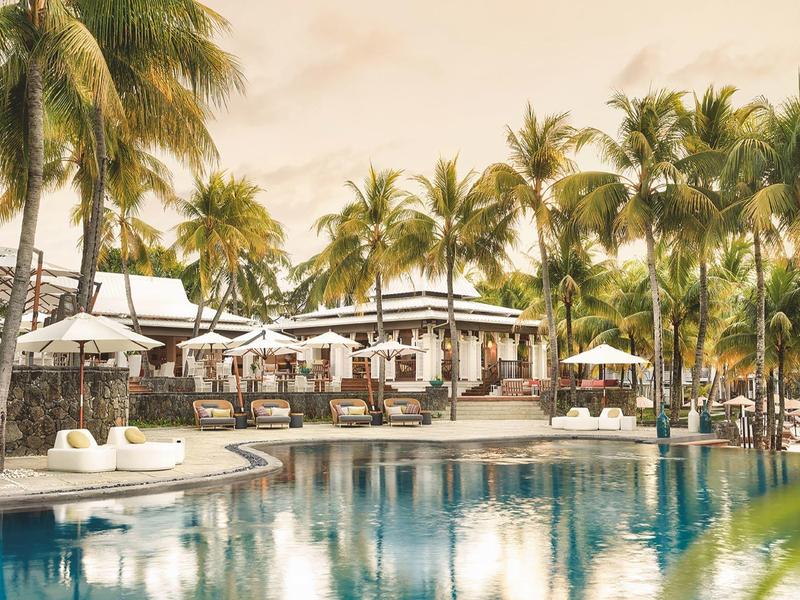 Tropický hotelový bazén s palmami a slunečníky v klidném prostředí.