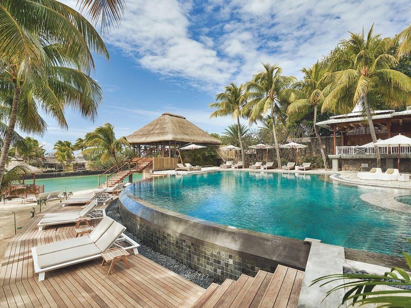 Kruhový hotelový bazén obklopený palmami a lehátky pod modrou oblohou.