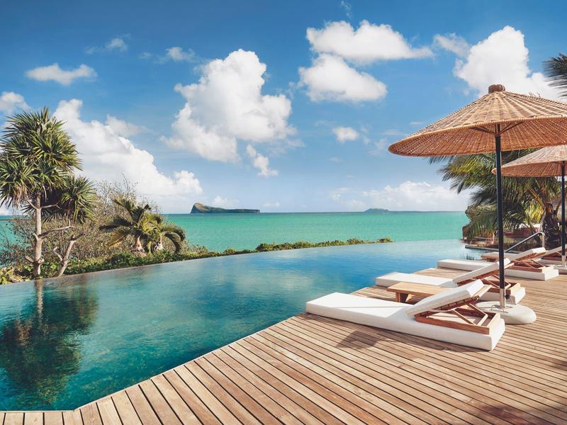 Infinity bazén s lehátky a slunečníky na dřevěné terase s výhledem na moře.