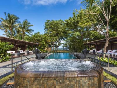Außenjacuzzi mit sprudelndem Wasser vor Pool, umgeben von Palmen und gemütlichen Liegen.