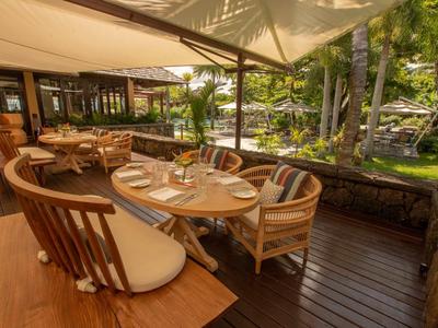 Restaurantterrasse mit Holzboden und runden Tischen, umgeben von grünem Garten und Bäumen.