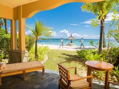 Blick von Terrasse mit Möbeln auf weißen Sandstrand, Palmen und türkisblaues Meer unter klarem Himmel.