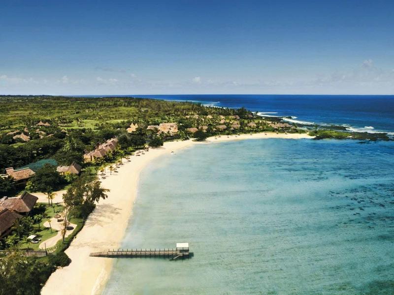 Strand mit weißem Sand, grünem Wald, blauer See und kleinem Holzsteg am Ufer.