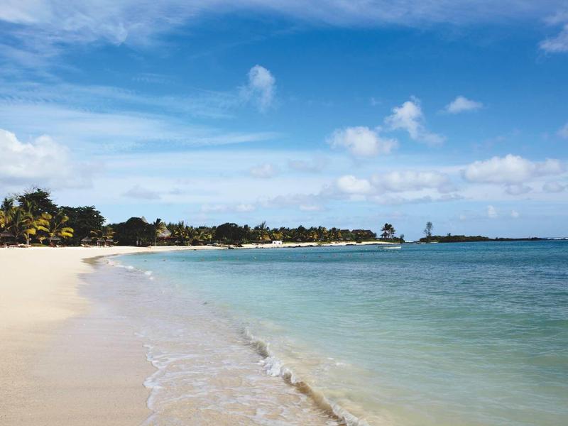 Feiner Sandstrand mit Palmen und klarem, türkisblauem Meer unter blauem Himmel mit Wolken.