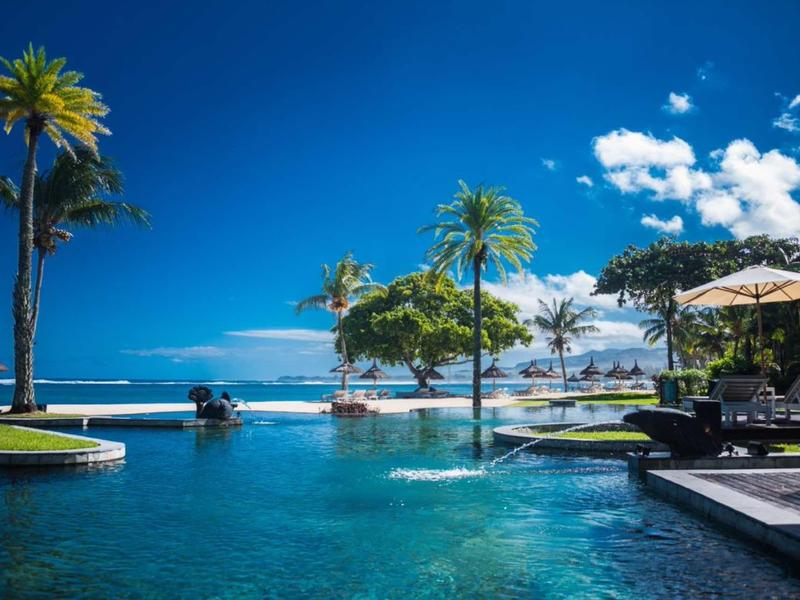 Luxuriöser Pool mit Palmen, Liegestühlen und blauem Himmel in tropischer Umgebung.