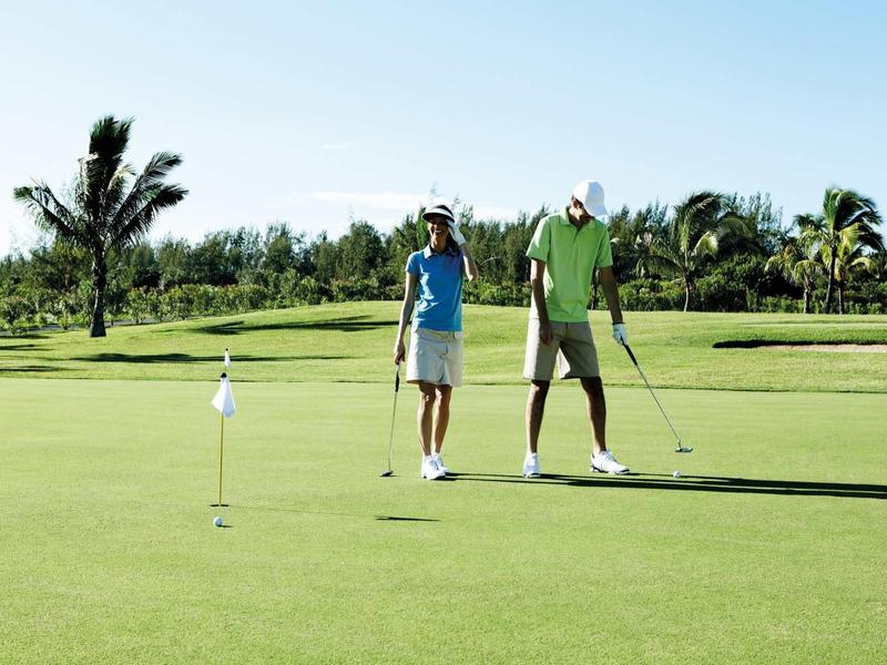 Zwei Golfer auf grünem Golfplatz, umgeben von Palmen und blauem Himmel.
