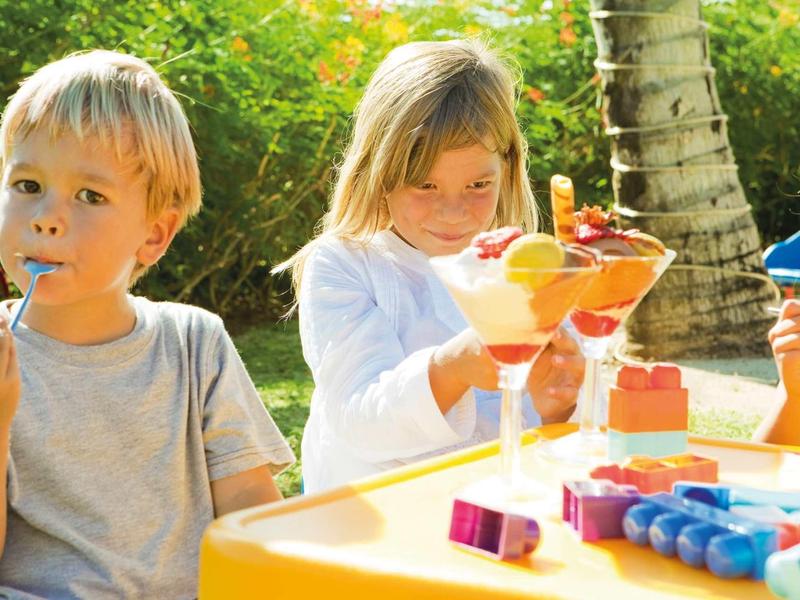 Kinder sitzen draußen am Tisch und essen Eiscreme bei sonnigem Wetter.