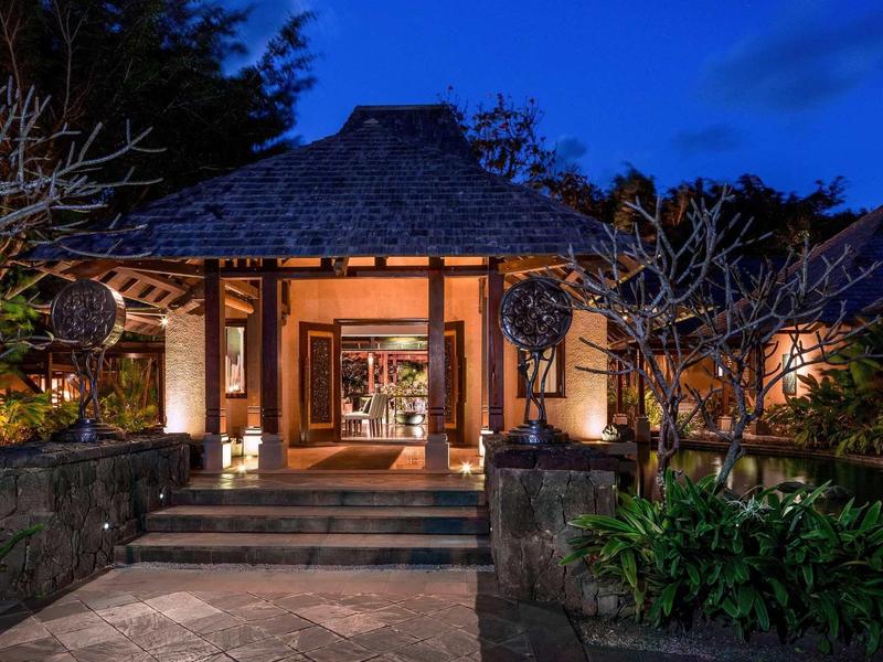 Traditionelles Balinesisches Haus mit Holzbau, Steintreppe und Beleuchtung in der Nacht.