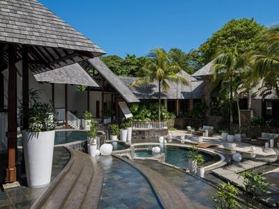 Hotel de lujo con piscina, sombrillas y vegetación tropical bajo un cielo despejado.