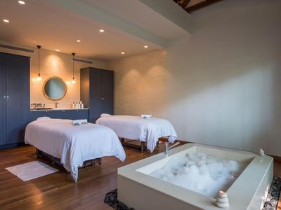 Sala de bienestar moderna con dos camillas cómodas y una bañera de espuma, iluminada con luz cálida.