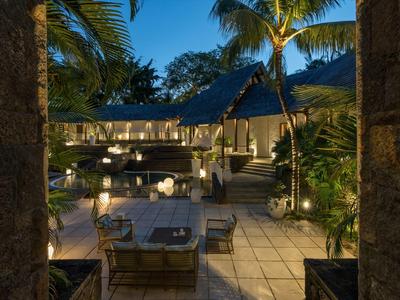 Terraza acogedora de hotel con mesas y sillas, rodeada de palmeras y faroles al anochecer.