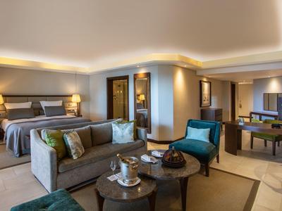 Habitación de hotel elegante con dos camas, área de estar moderna y iluminación ambiental.