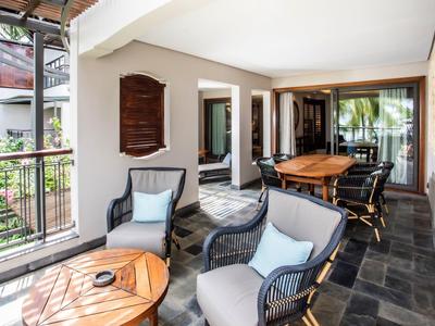 Balcón cubierto con área de asientos y mesa de madera, rodeado de barandilla de vidrio y acceso interior.