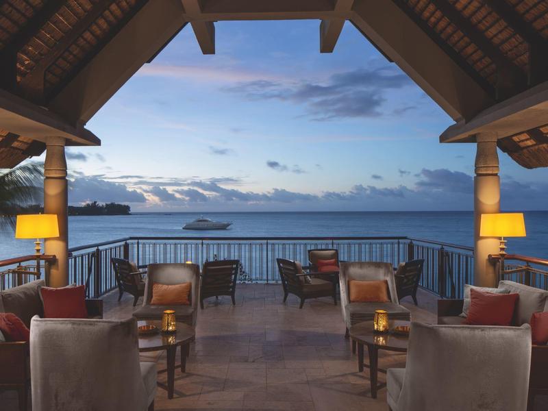 Terraza acogedora de hotel con vista al mar y al atardecer, sillas y lámparas visibles.