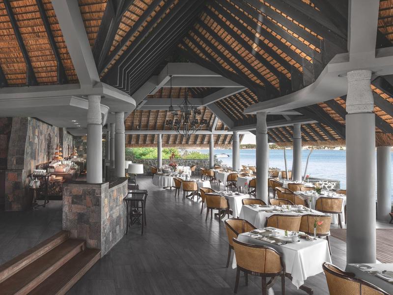 Amplio restaurante con techo de madera, columnas y mesas preparadas con vistas al agua.