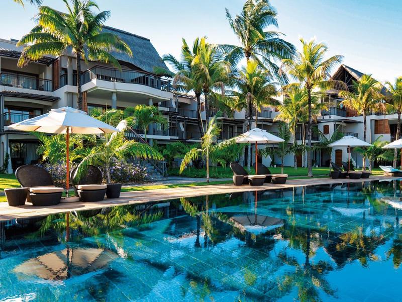 Piscina azul clara frente a un hotel con tumbonas y palmeras en un día soleado