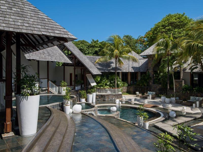 Hotel de lujo con piscina, sombrillas y vegetación tropical bajo un cielo despejado.