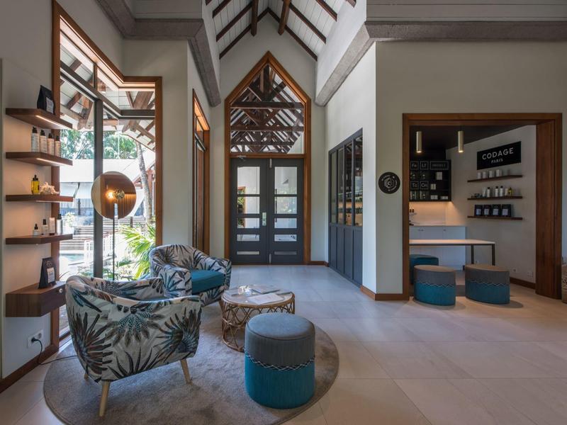 Área luminosa del vestíbulo del hotel con sillones cómodos, taburetes y marco de madera decorativo en la puerta.