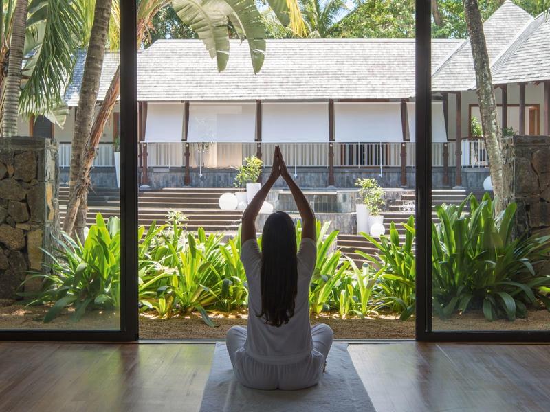 Persona haciendo yoga frente a una terraza y jardín tropical en un hotel.