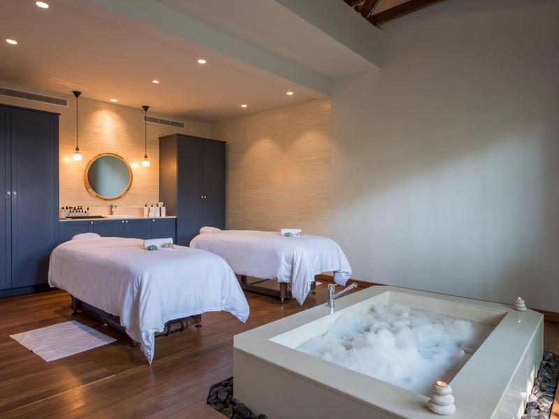 Sala de bienestar moderna con dos camillas cómodas y una bañera de espuma, iluminada con luz cálida.