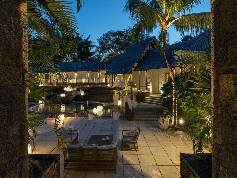 Terraza acogedora de hotel con mesas y sillas, rodeada de palmeras y faroles al anochecer.