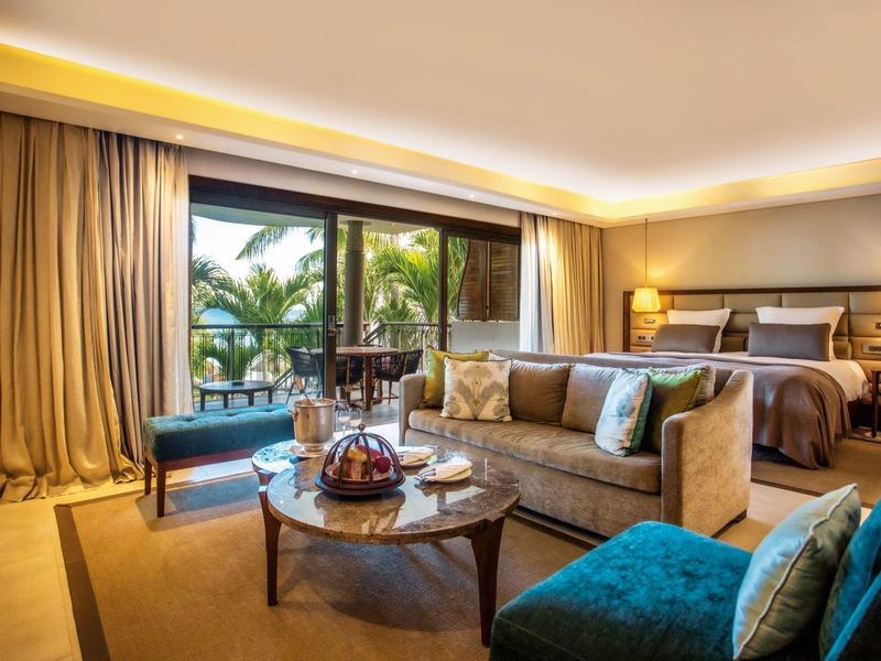 Habitación de hotel lujosa con área de descanso, cama grande y vista a una terraza con palmeras.