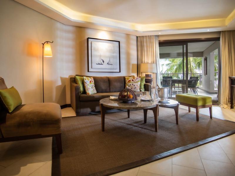 Habitación de hotel acogedora con sofá, mesa de café, alfombra y acceso a balcón con plantas.