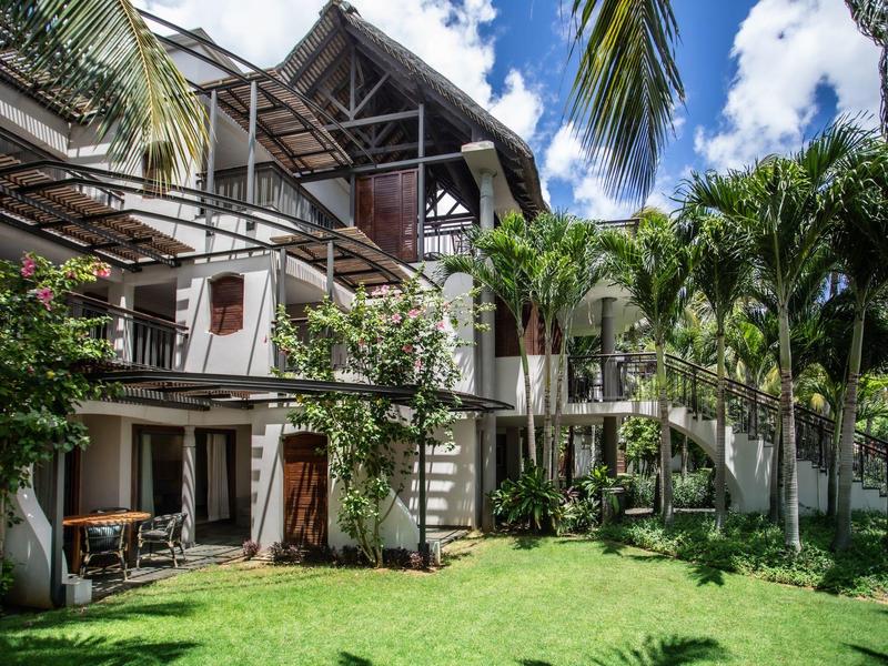 Hotel con jardín tropical, dos pisos y terrazas de madera bajo cielo azul