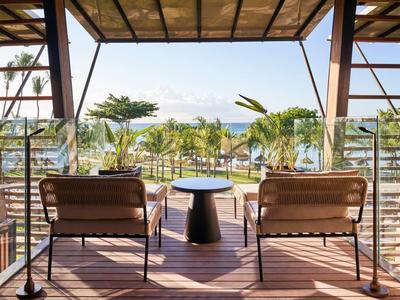 Blick auf Meer und Palmen von überdachter Holzterrasse mit Stühlen und kleinem Tisch.