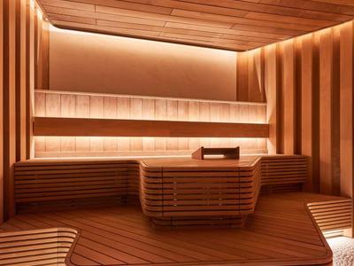 Moderne Sauna mit warmem Holz, indirekter Beleuchtung und gestreiften Holzmöbeln in warmem Licht.