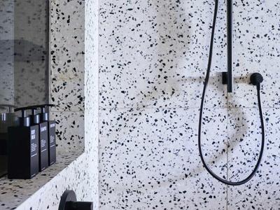 Moderne Dusche mit schwarz-matten Armaturen und weißem Mosaikfliesenmuster an Wand und Boden.